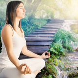 A woman meditating outdoors on a wooden platform over a waterfall in a sunny, green setting, representing the focused intention rite.