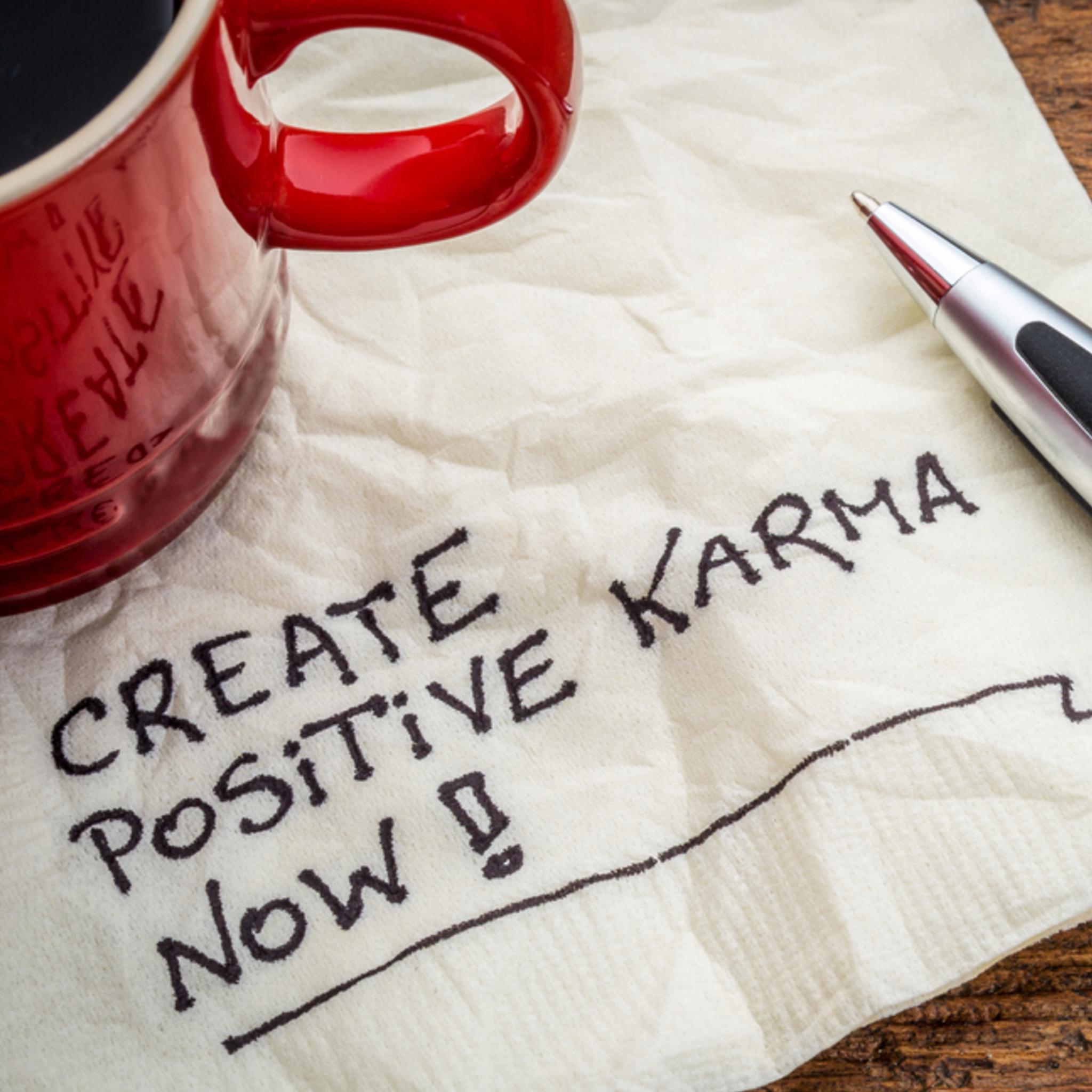 Red mug, pen, and napkin with 'Create Positive Karma Now' text on a wooden surface.