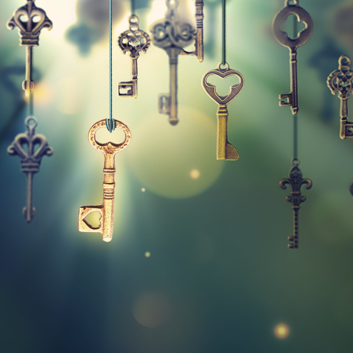 Vintage brass keys hanging against a soft green and golden bokeh background.