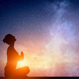 A dark silhouette of a person sitting in a cross-legged position with hands in a prayer pose, looking upward. The figure is brightly backlit by an intense orange and yellow glowing light at the base, contrasting with a deep blue, starry cosmic sky above.