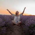 Woman sitting cross-legged in a purple lavender field at sunset representing manifestation path alignment dedication.