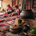 Traditional clay pots heating over an open fire on a hearth, with women in colourful Andean clothing sitting behind.