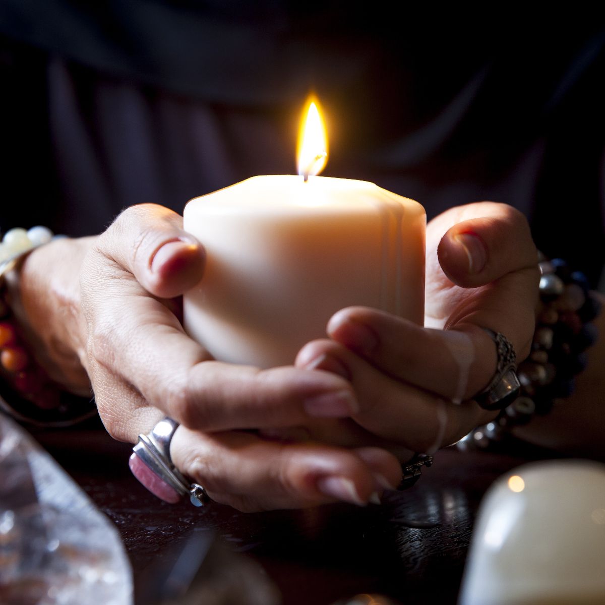 Hands holding a lit candle with a dark mystical background.