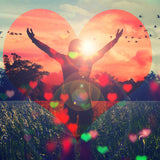 A double-exposure image where a person with their arms raised in a gesture of freedom stands silhouetted against a sunset, surrounded by trees and a field. The scene is framed inside a large, glowing red heart shape, with smaller hearts scattered in the foreground.