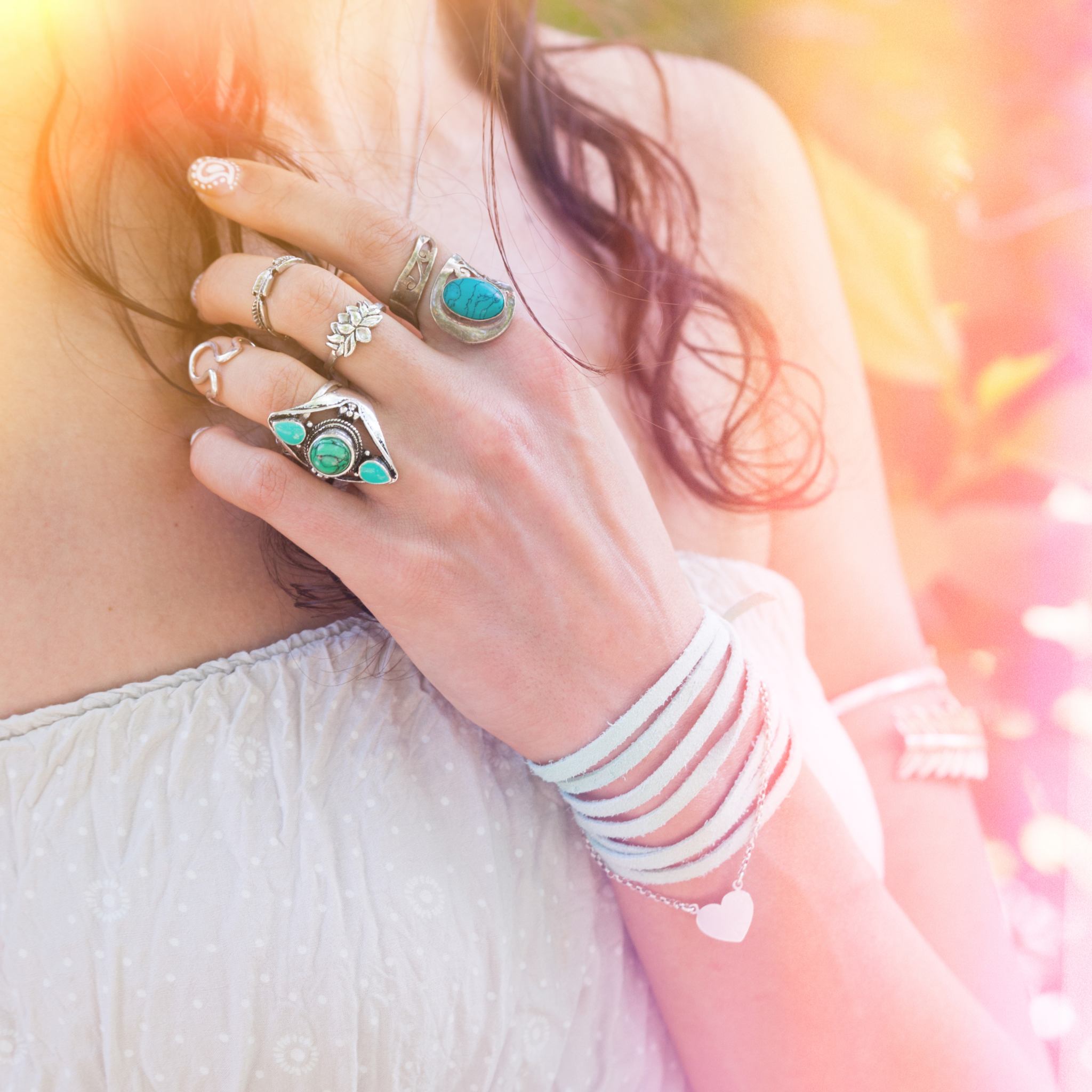 Close-up of a person's hand wearing multiple rings and bracelets with a blurred, colourful light rays background.