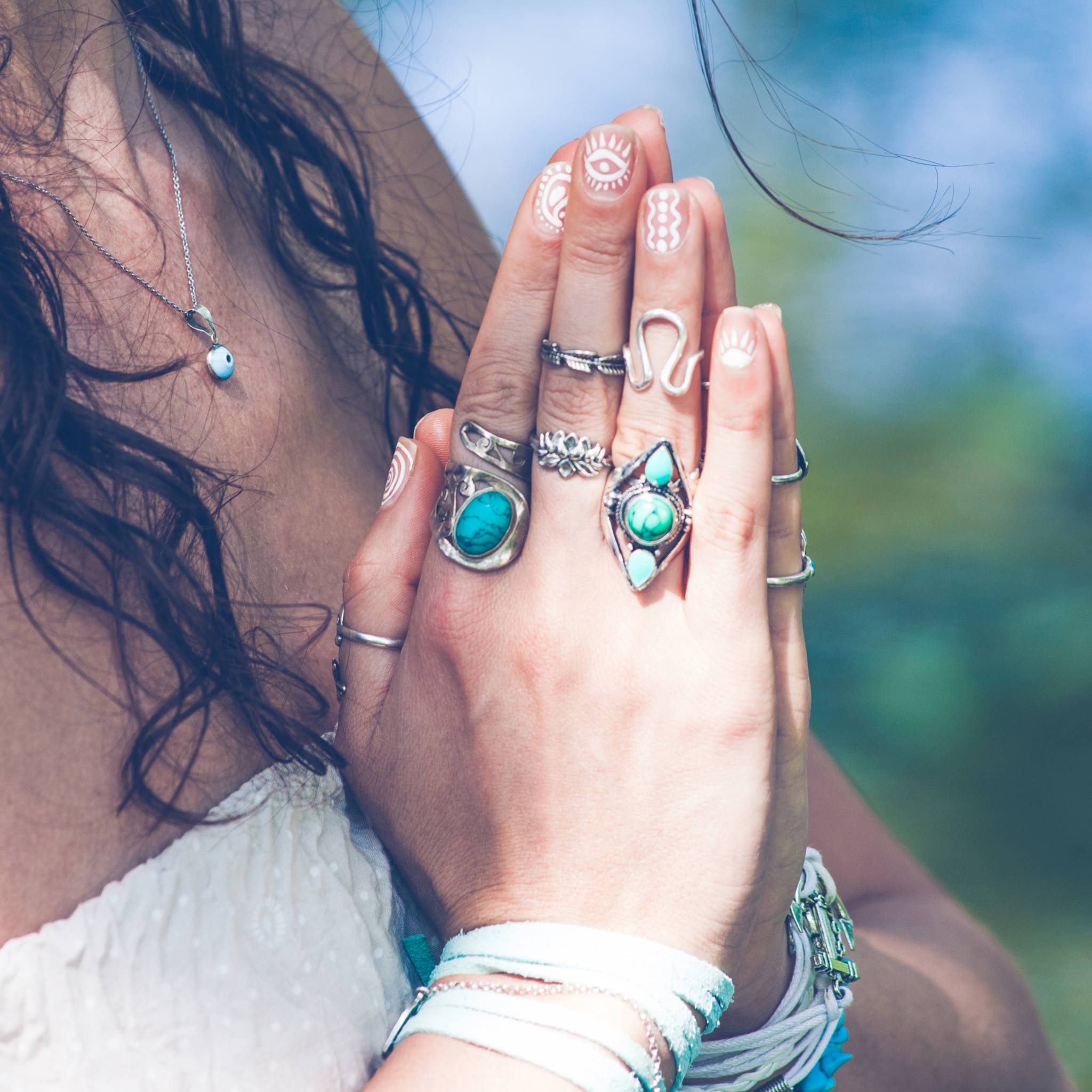 Two hands in prayer adorned with many silver and turquoise rings.