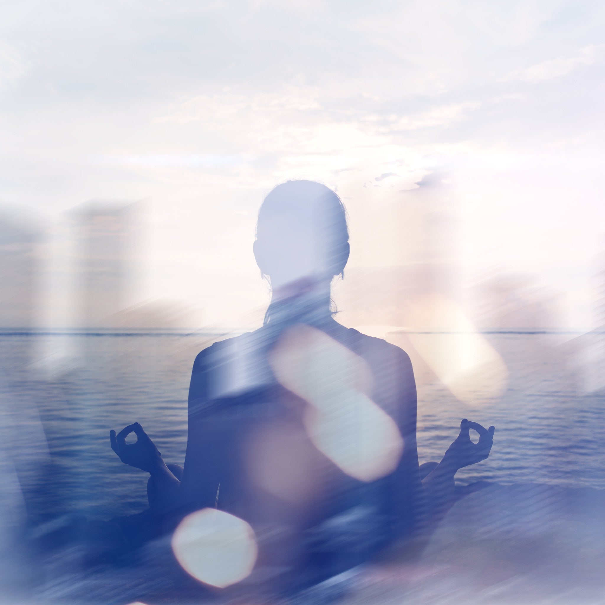 Person meditating by a body of water with a blurred background.