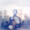 Person meditating by a body of water with a blurred background.