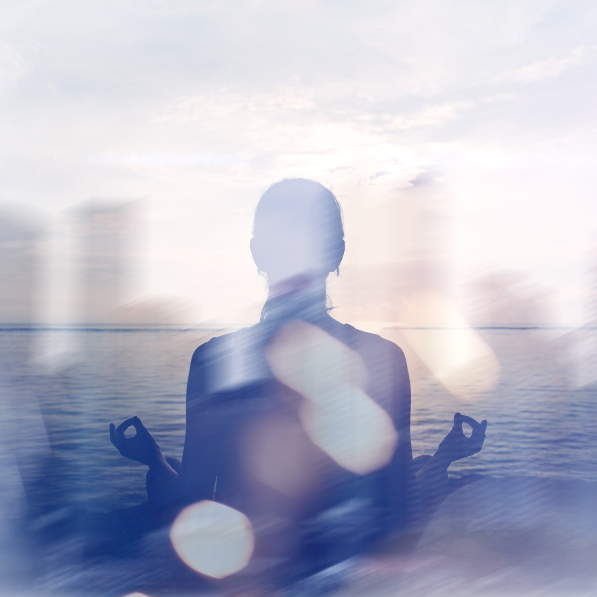 Person meditating by a body of water with a blurred background.