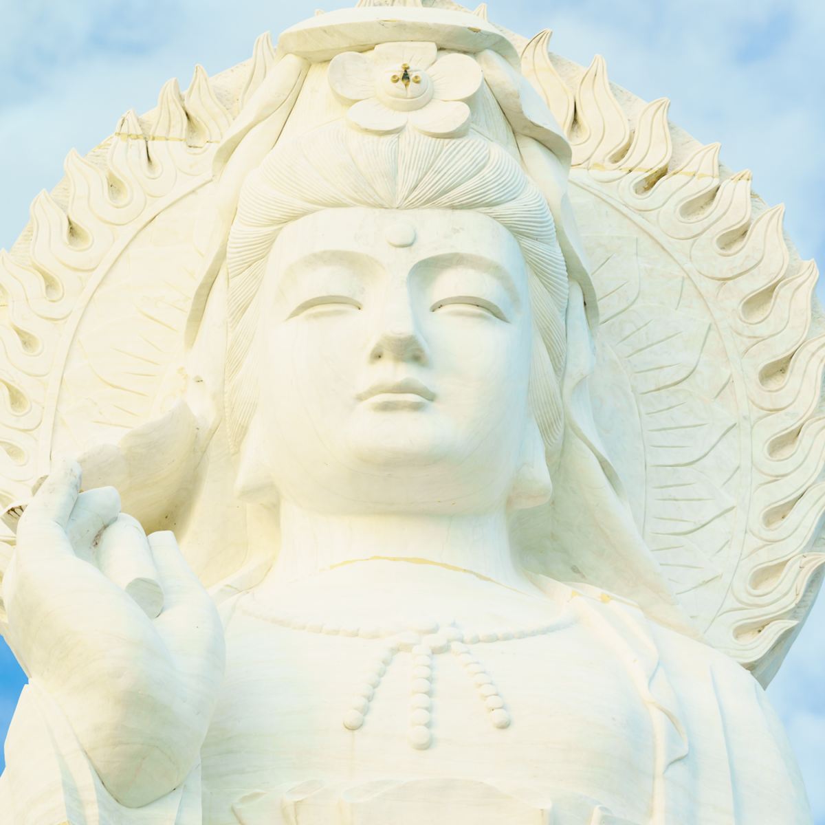 White marble Quan Yin statue with intricate details against a clear blue sky.