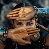 A person with tribal jewellery and makeup holding hands over their face.