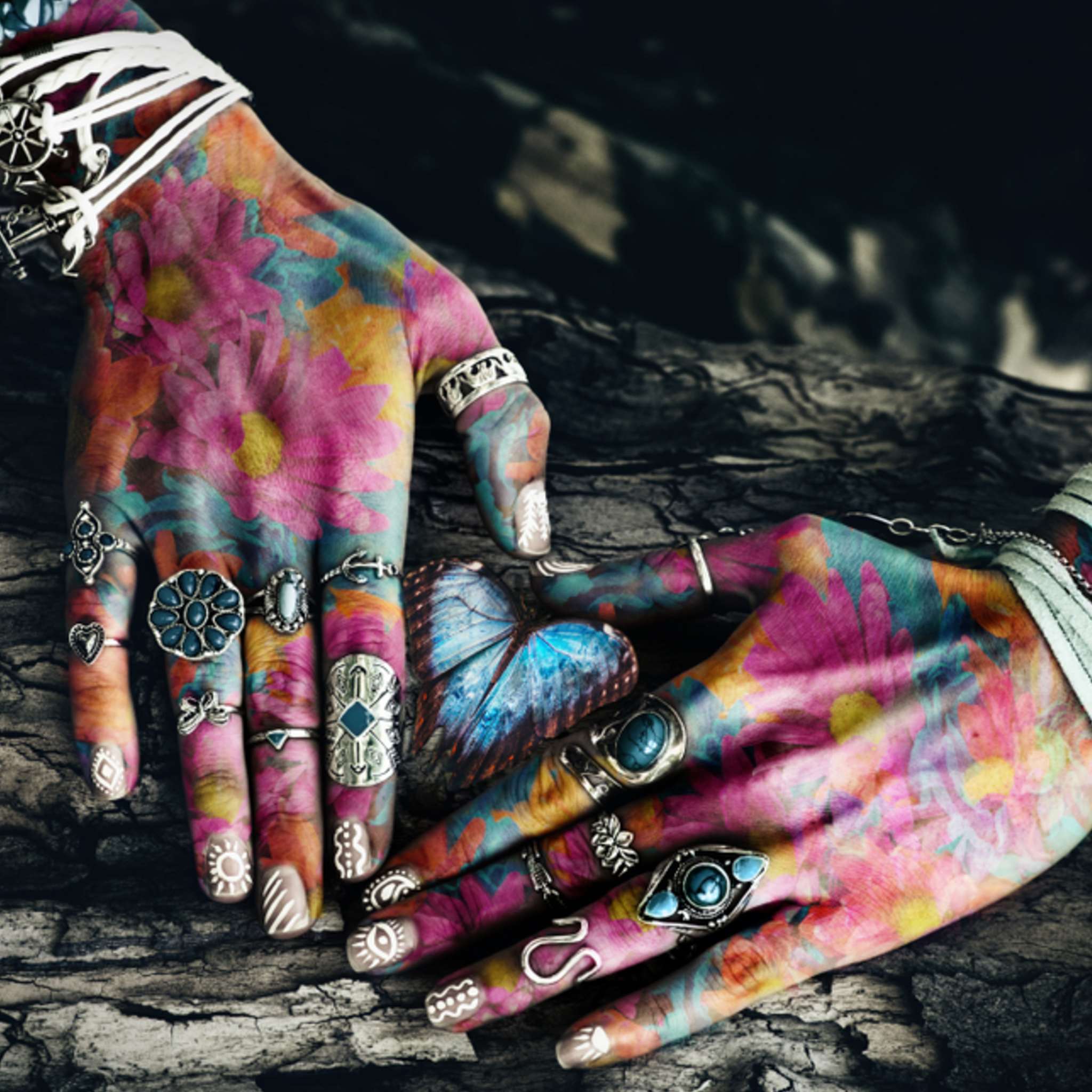 Colourful hands with tattoos and jewellery on a dark textured background.