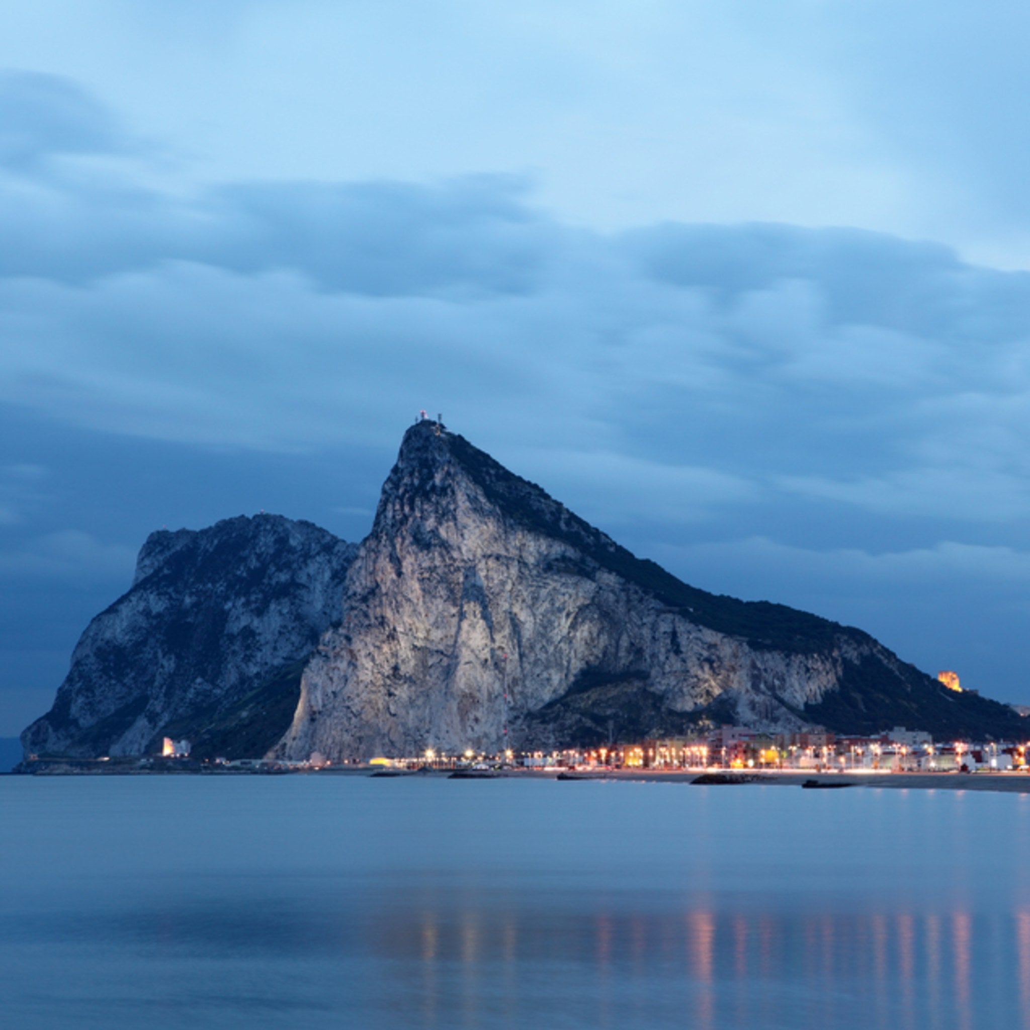 Rock of Gibraltar at dusk with lights reflecting on the water.
