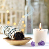 Sapce clearing sage bundle on a dish with a lit candle and crystals.