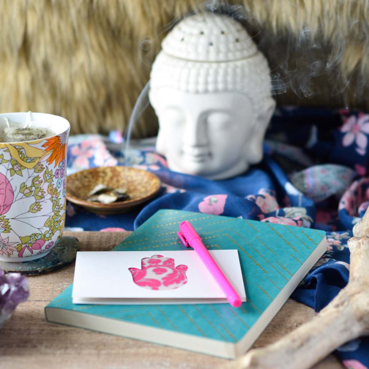Tea cup, notebook, and pen on a table with a Buddha statue in the background.