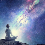 Silhouette of a figure sitting in meditation on a rocky outcrop, looking up at a vast, bright, purple and blue cosmic galaxy.