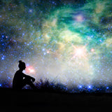 A beautiful silhouette of a person sitting alone on a dark, grassy mound, looking upwards at a vast, bright, and colourful night sky filled with countless stars, a brilliant central nebula, and a large starburst effect. This celestial imagery signifies the cosmic origin and connection of the starseed path alignment dedication.