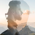 Double exposure of a person with glasses and mountains at sunset.