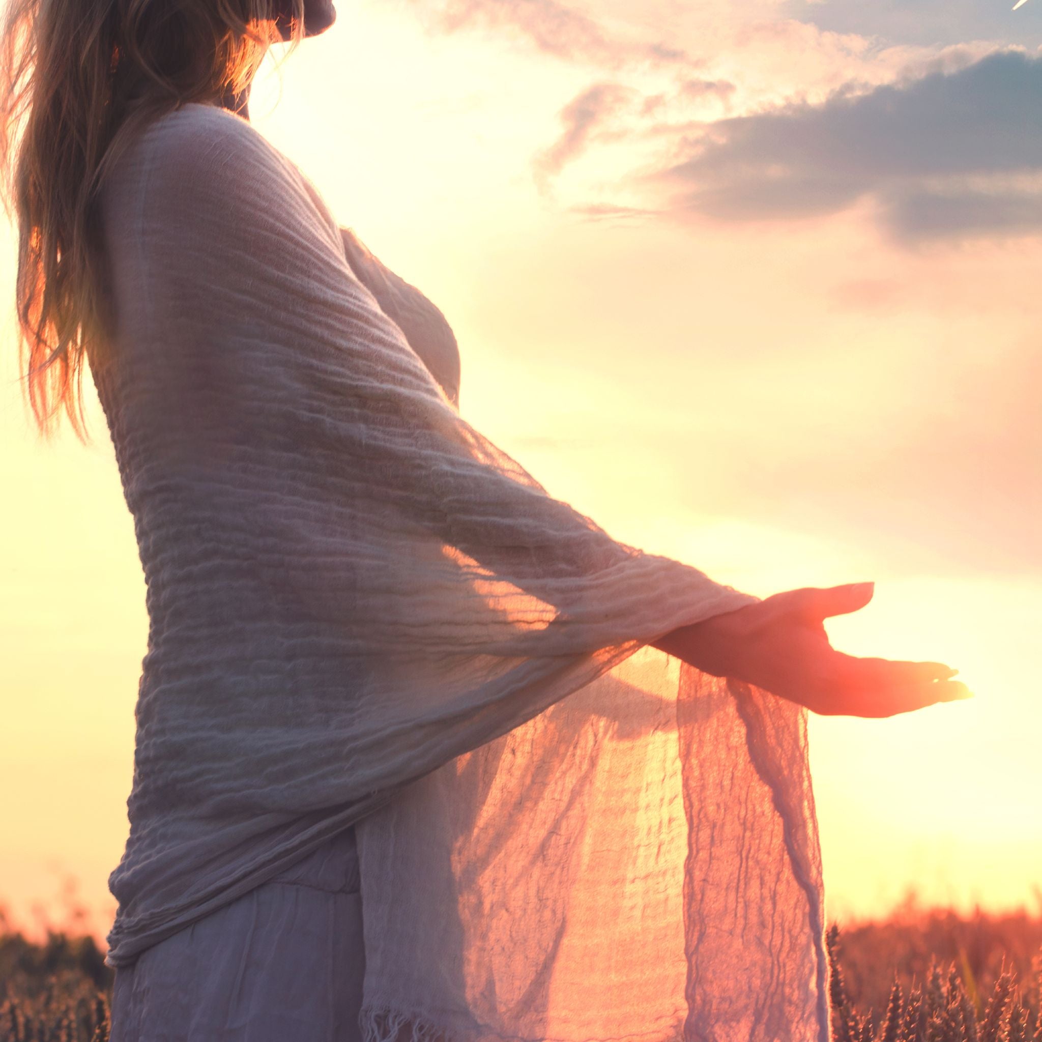A woman in a white, flowing scarf stands in a field with her arms open at sunset, representing the peaceful surrender rite.