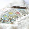 A close-up, soft-focus photograph of four classic Tarot cards laid out on a white, fluffy rug or throw, alongside a flickering tea light and a feather. The visible cards include The Star and The World, representing the focus on intuition and clarity in the Tarot reader path alignment dedication.