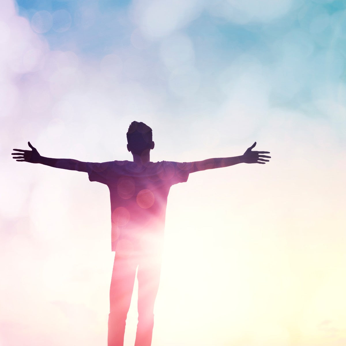Person with arms outstretched against a colourful sky.