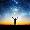 A person's silhouette with arms raised towards a vast, starry sky at sunset, symbolising empowerment and spiritual connection.
