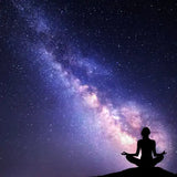 A silhouette of a person in a meditation pose against a night sky filled with stars and the milky way galaxy.