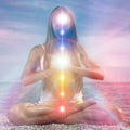 Person meditating on a beach with an illuminated, vertically aligned column of chakras and kundalini spiritual light.
