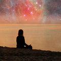 A silhouette of a person in meditation on a beach, with a celestial nebula and stars in the sky, symbolising spiritual connection and cosmic alignment.