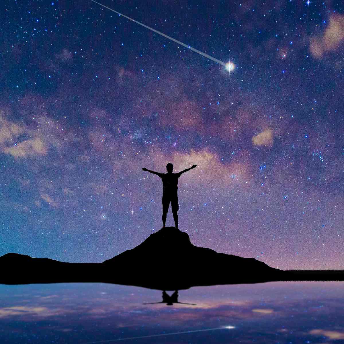 Silhouette of a person standing atop a hill with open arms beneath a starry night sky and shooting star reflected in calm water.