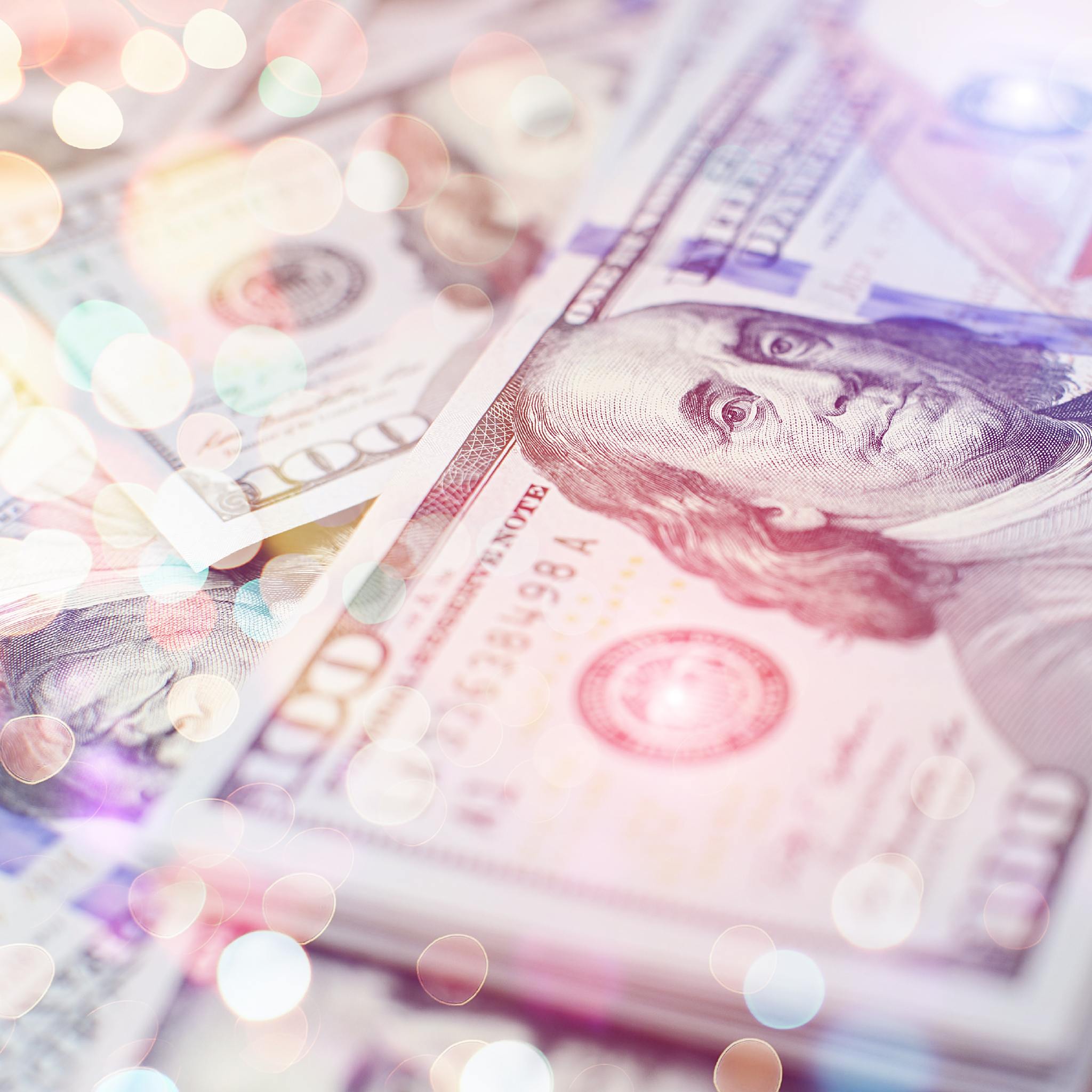 A close-up of a stack of US one-hundred dollar bills, with colourful circular bokeh lights, representing third eye money enhancement.